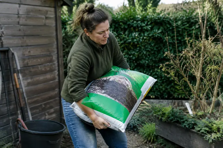 Jardinier soulevant un sac de quarante litres de terreau lourd dans son jardin